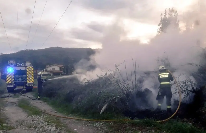 Los bomberos extinguen el fuego junto al tendido eléctrico en Somahoz.