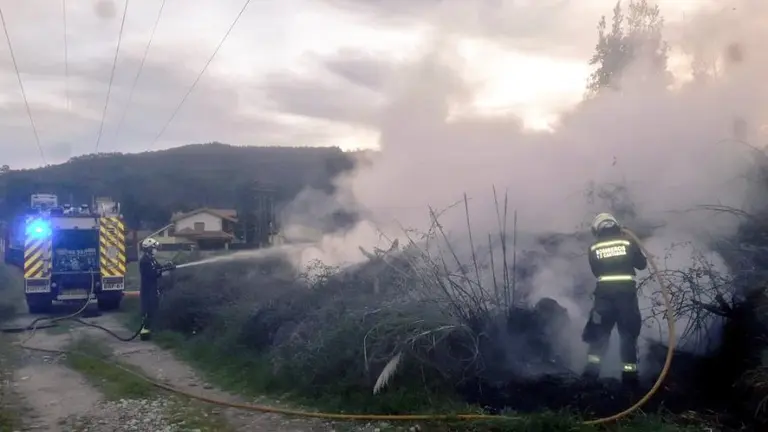 Los bomberos extinguen el fuego junto al tendido eléctrico en Somahoz.